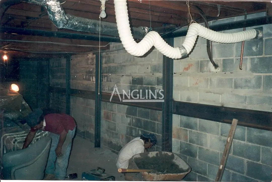 steel support beams in a basement of a bulding and with cracks between the bricks filled, there are two anglin employees working next to it
