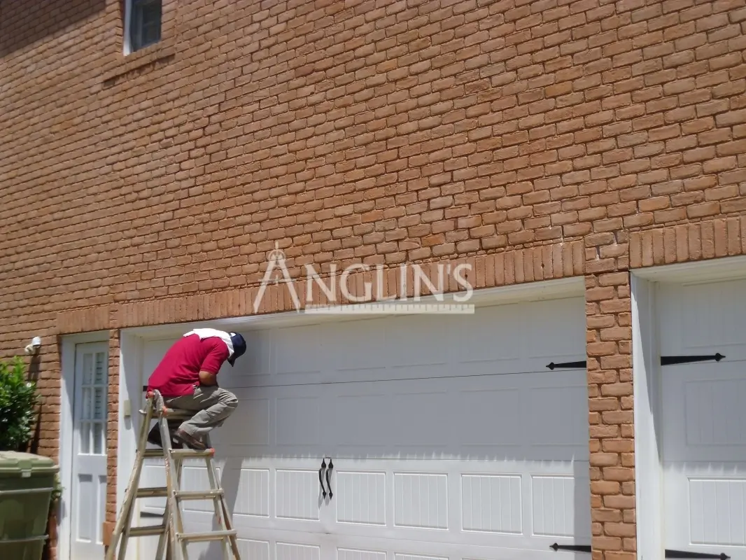 anglin's employee sitting on the top of the ladder while fixing the garage door